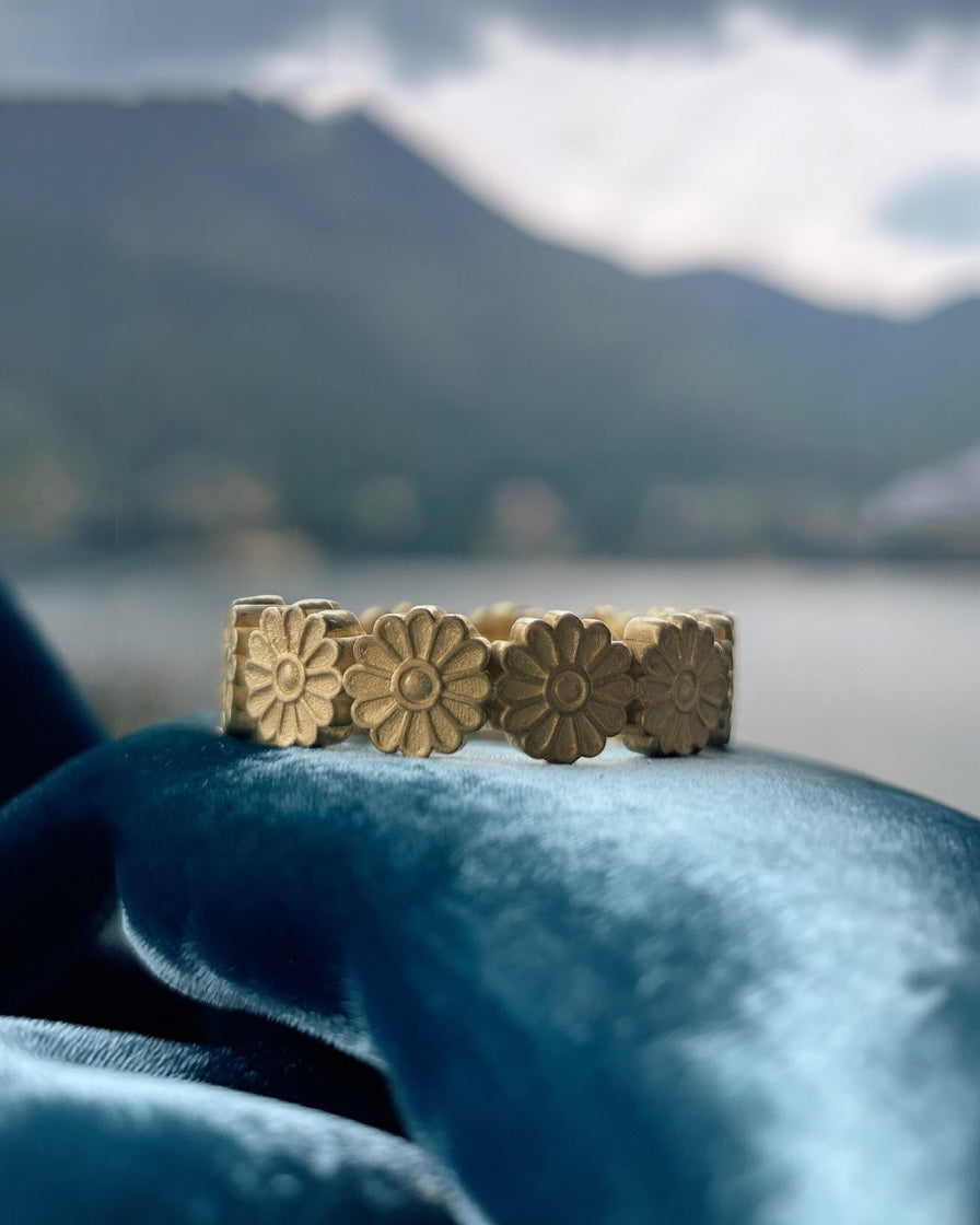 Gold floral Ring on a blue fabric with a blurred natural background