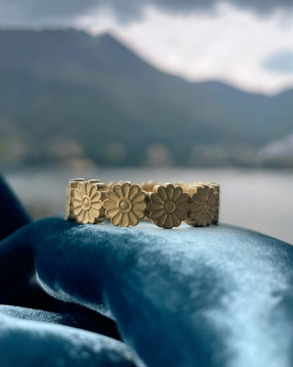Gold floral Ring on a blue fabric with a blurred natural background
