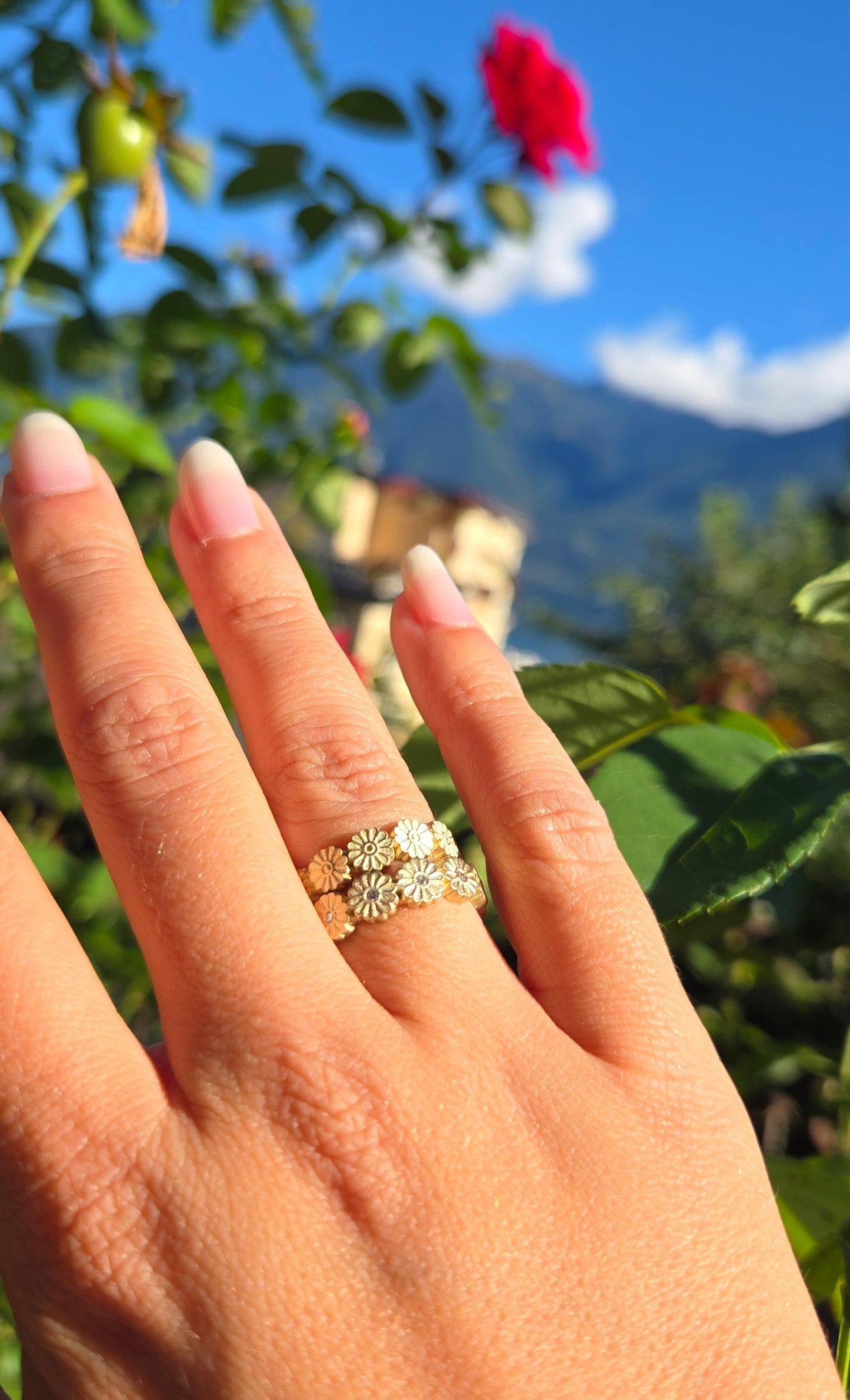 Hand wearing a diamond ring with a blurred background of greenery and blue sky