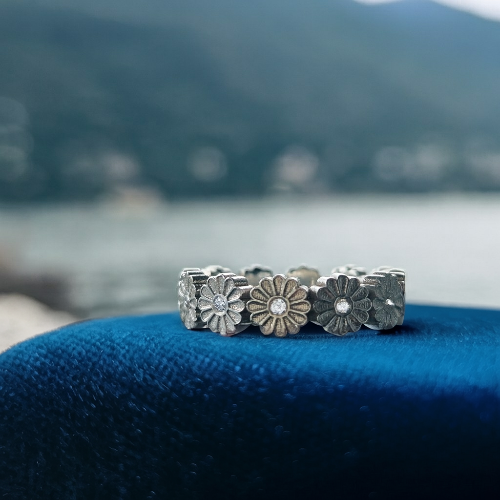 Three silver floral rings with embedded stones on a blue cushion with a blurred natural background