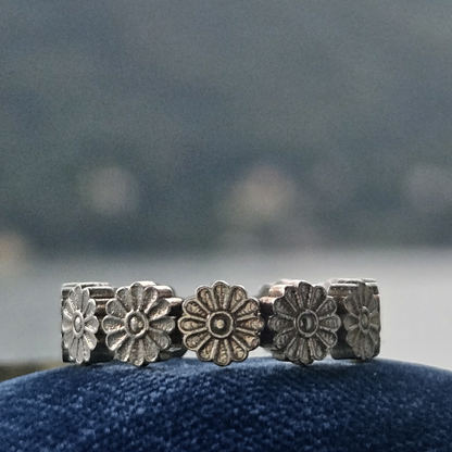Silver floral ring on a blue cushion with a blurred natural background